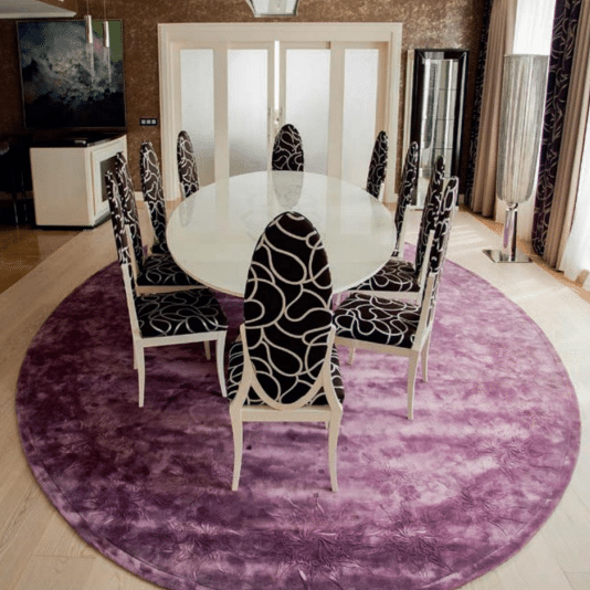 Modern dining room with round purple area carpet under oval table and black patterned chairs