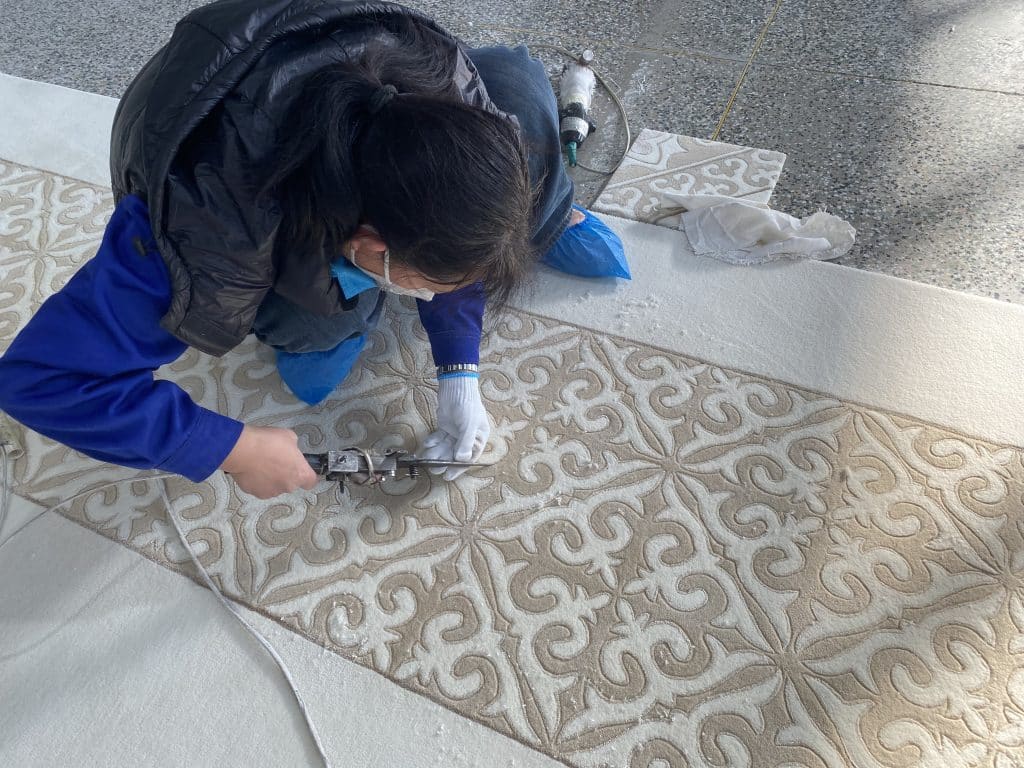 Artisan using electric trimmer on beige and white scrollwork hand knotted carpet during final surface shaping