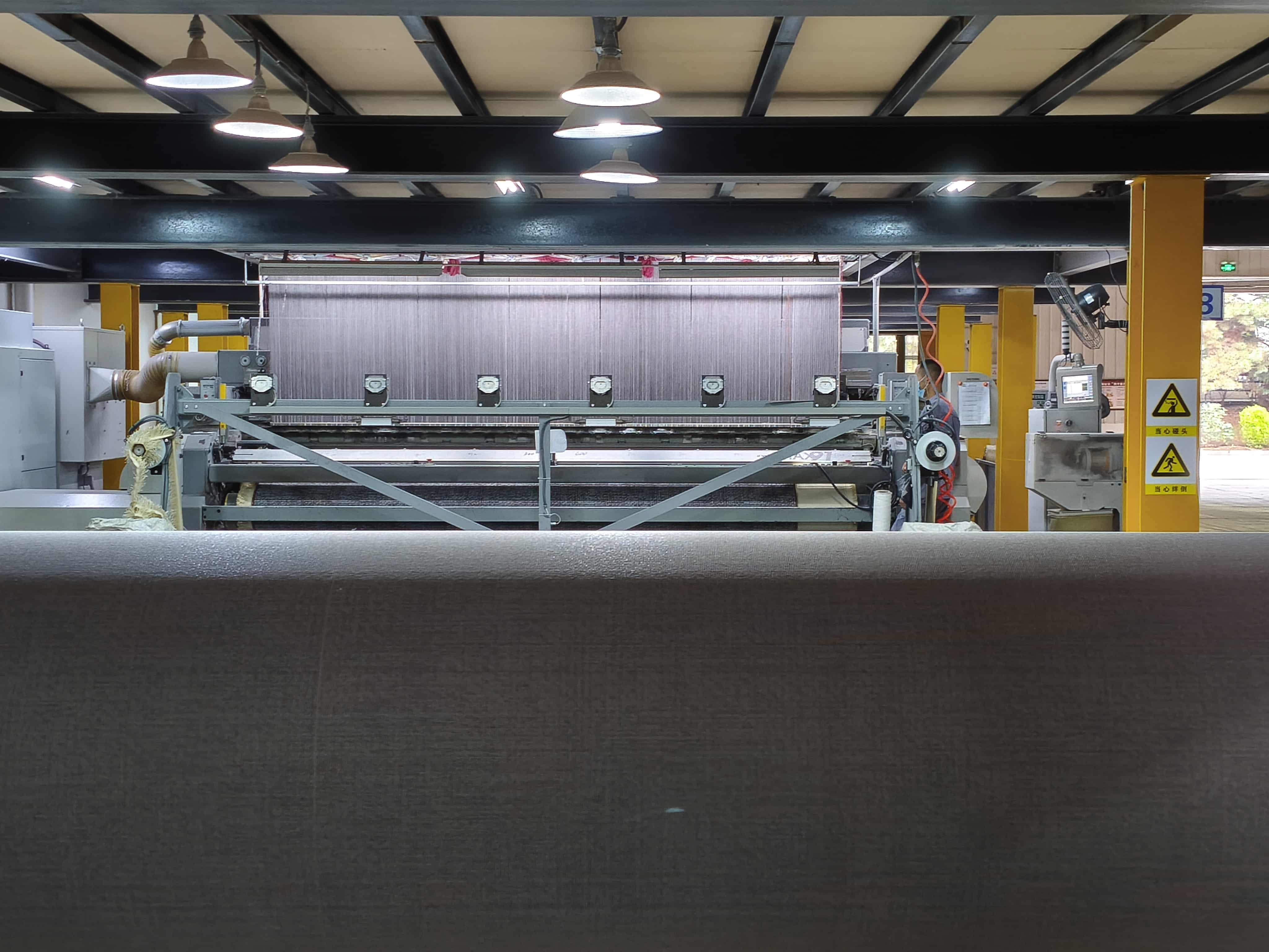 Automated wall-to-wall carpet weaving machine with rollers and digital interface in production workshop