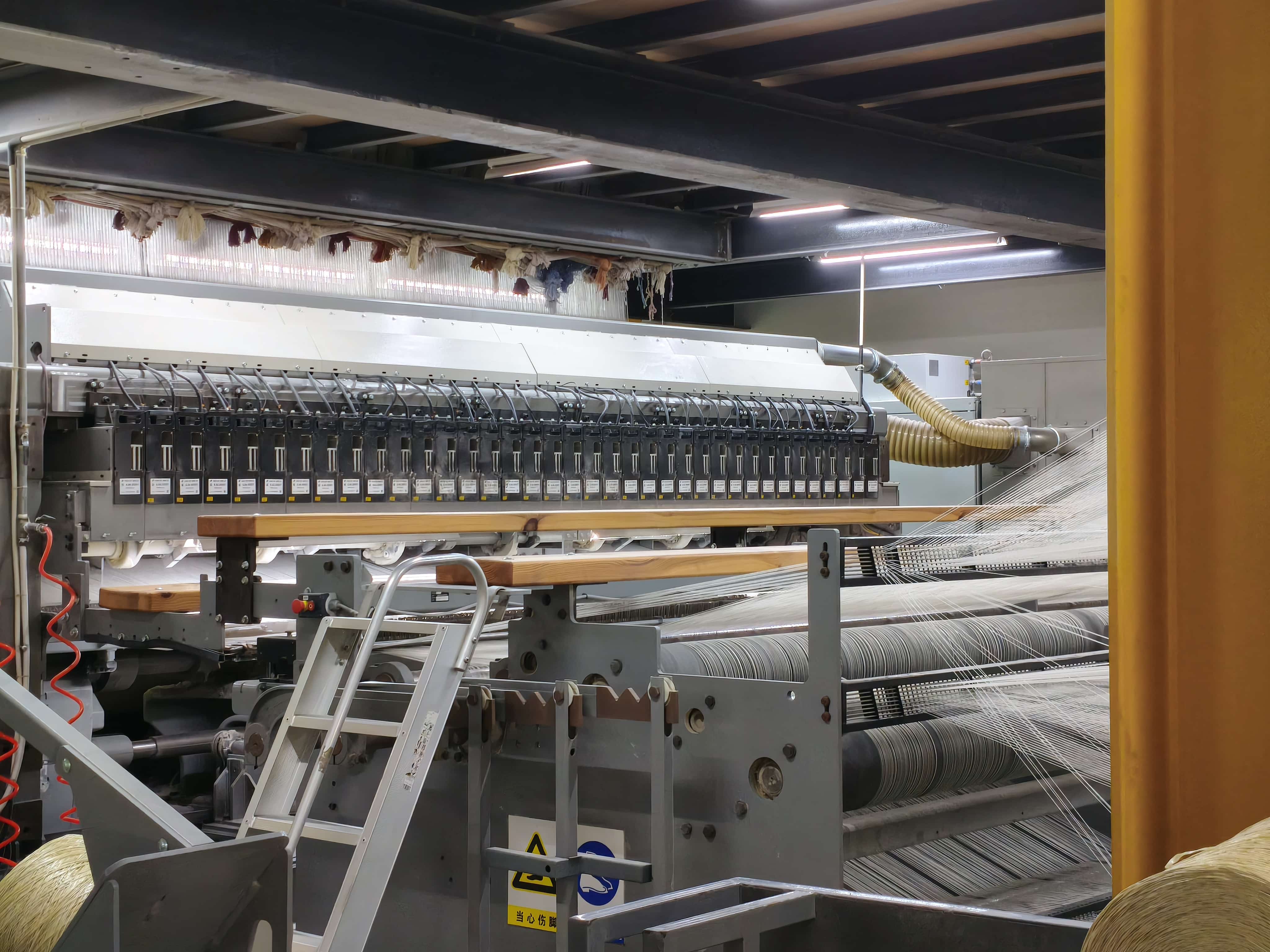 Side view of weaving equipment in wall-to-wall carpet factory with spools and yarn tension system