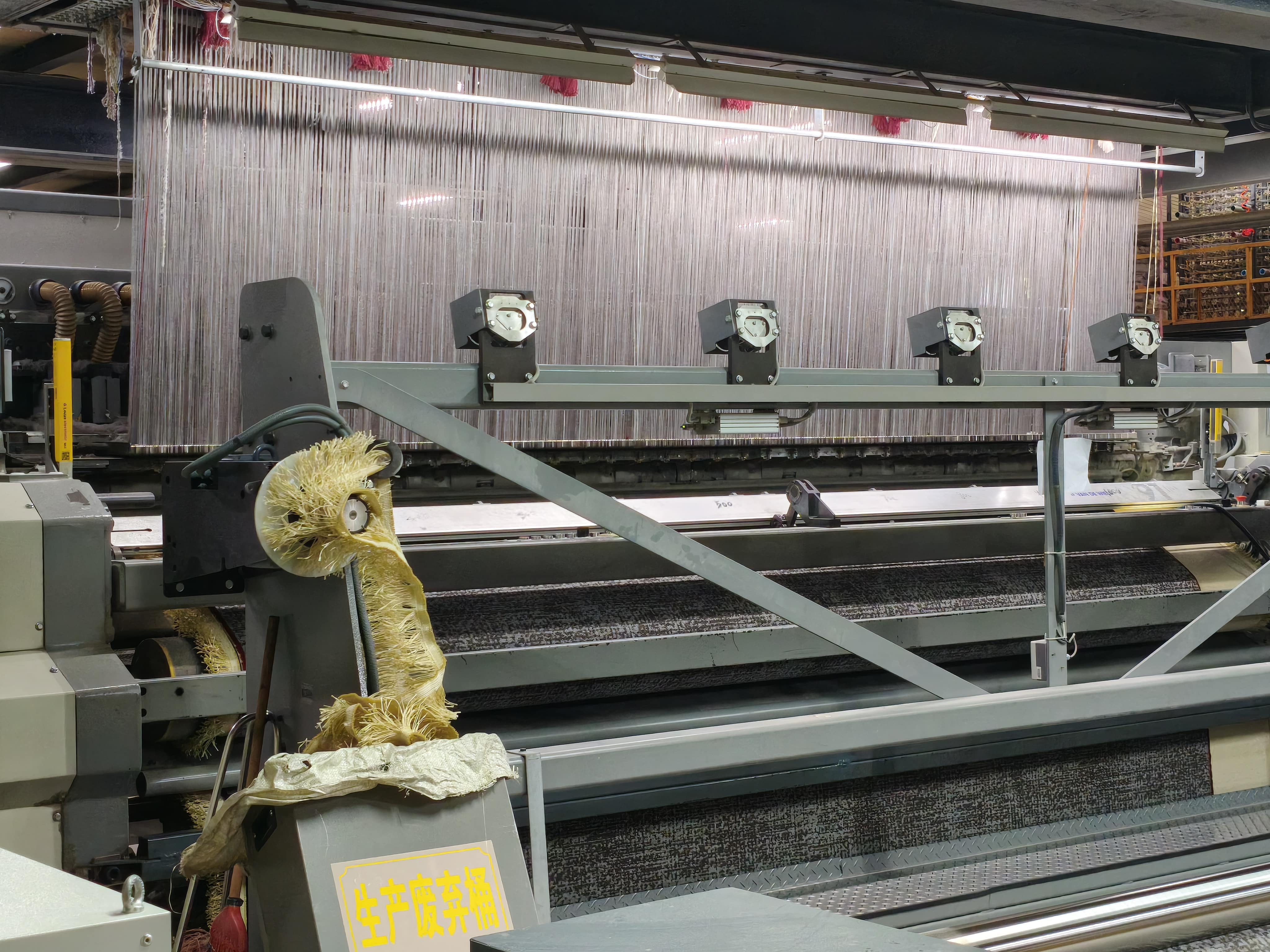 Close-up of industrial carpet machine with light grid and tensioned yarns during weaving