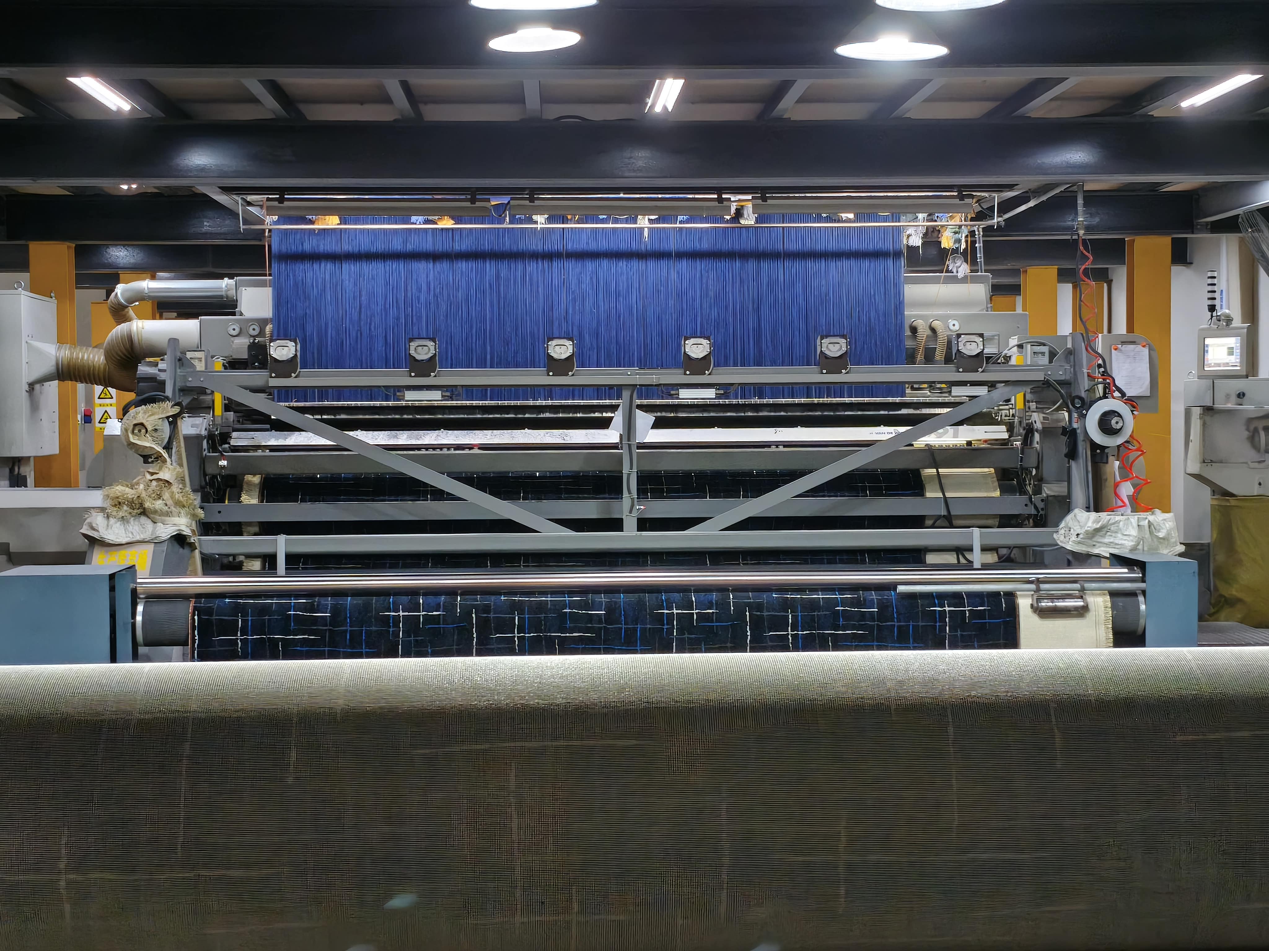 Wall-to-wall carpet production machine threading colored yarn through tension guides and rollers