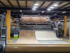An Axminster carpet with a decorative swirl pattern being released from an automated weaving machine
