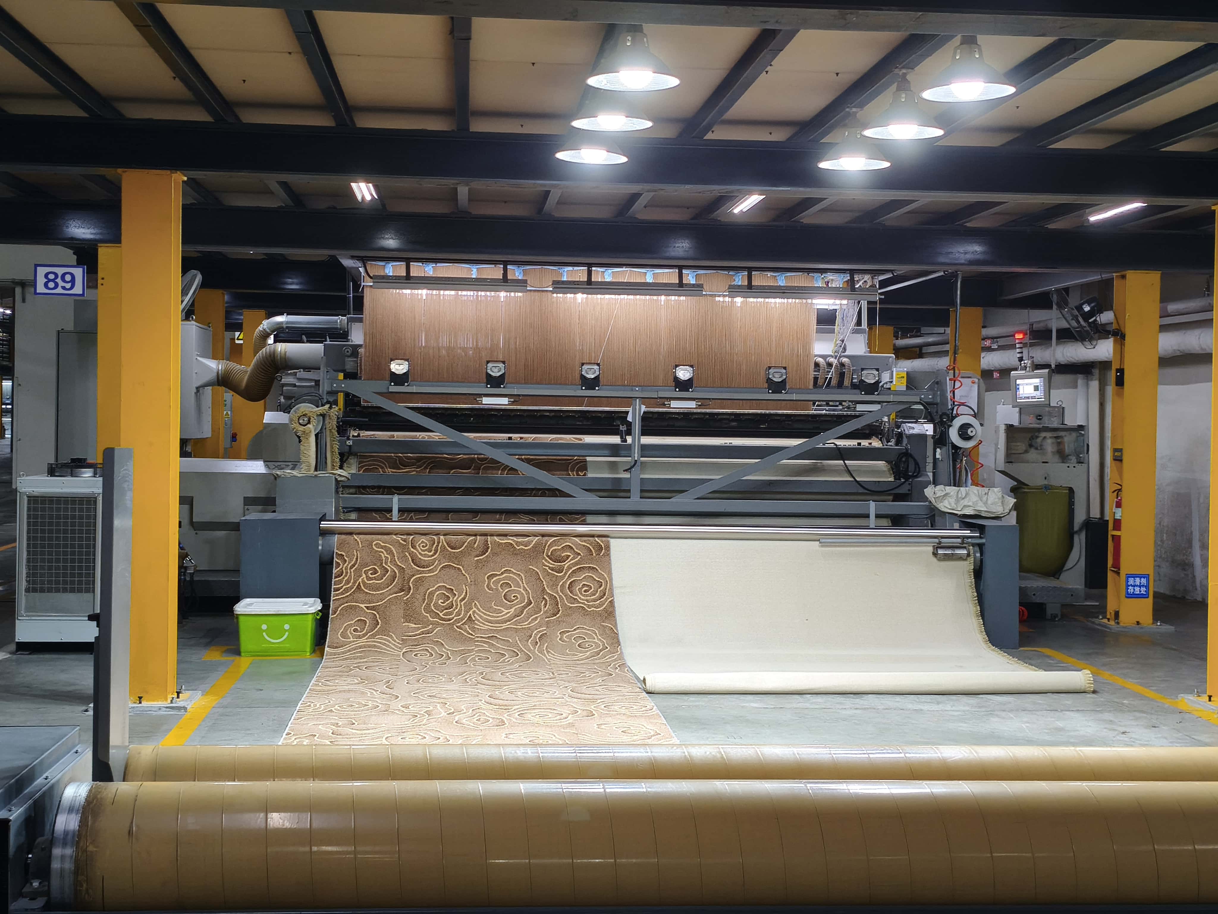 An Axminster carpet with a decorative swirl pattern being released from an automated weaving machine
