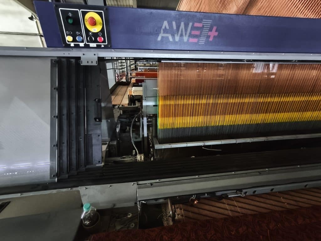 Close-up of yarn bed and control interface on Wilton loom with aligned orange and yellow yarns