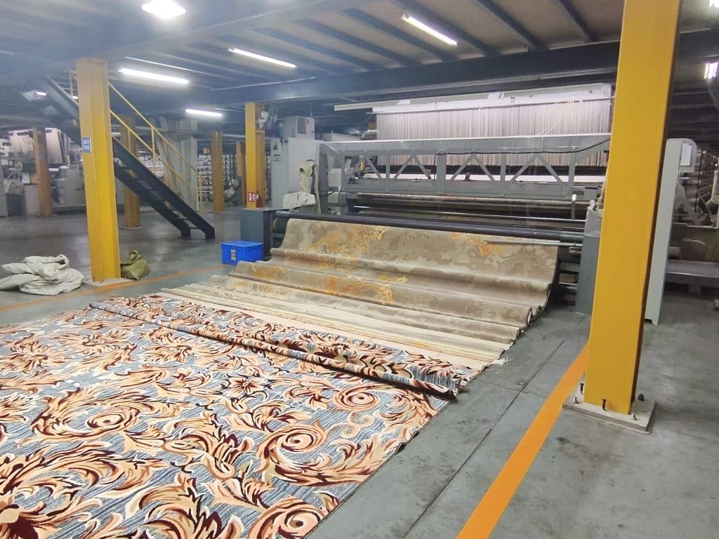 Qianqiao Axminster weaving machine outputting layered patterned carpets onto the workshop floor