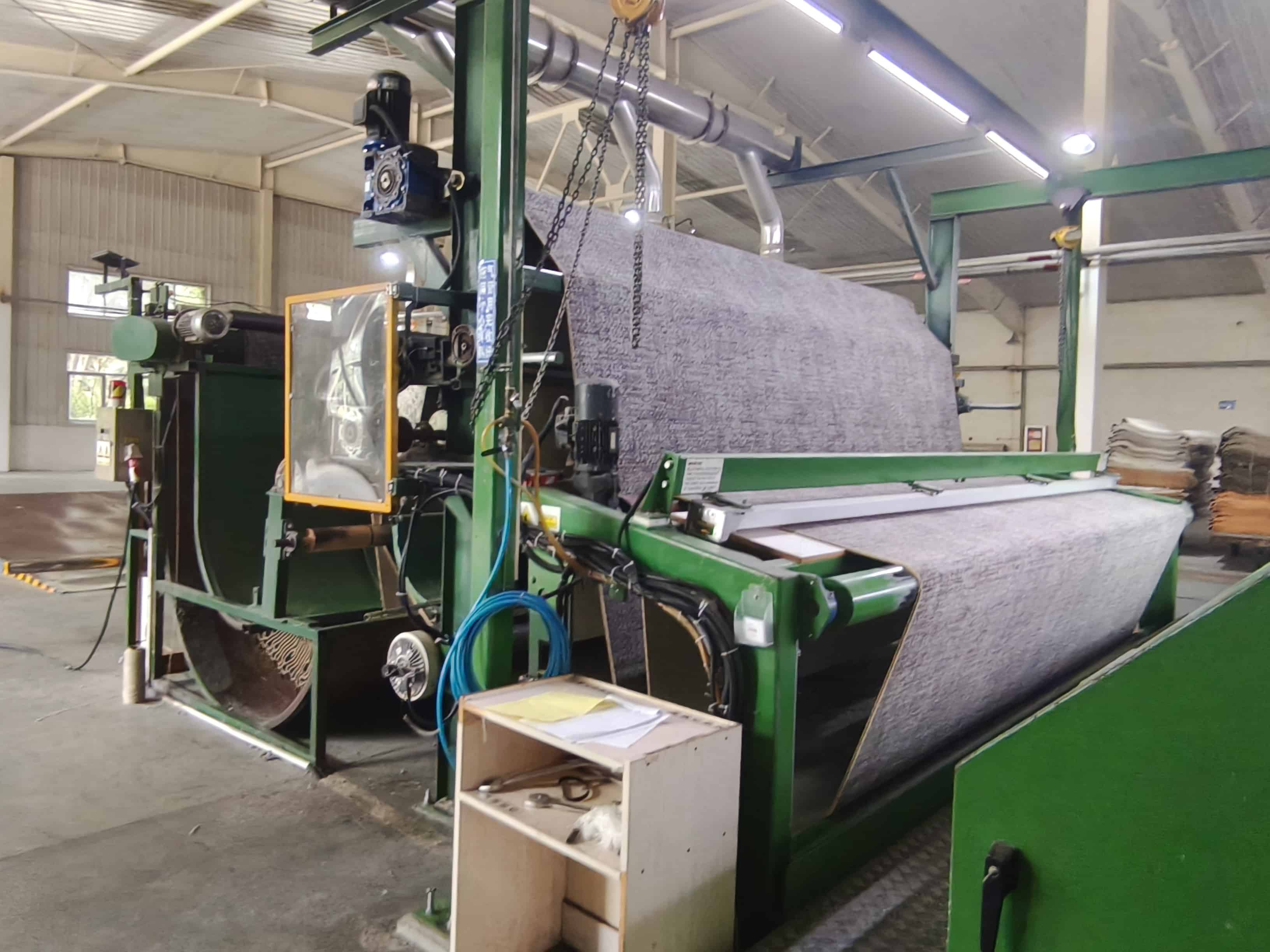 Printed carpet roll exiting an automated production line with control panel and compressed air piping