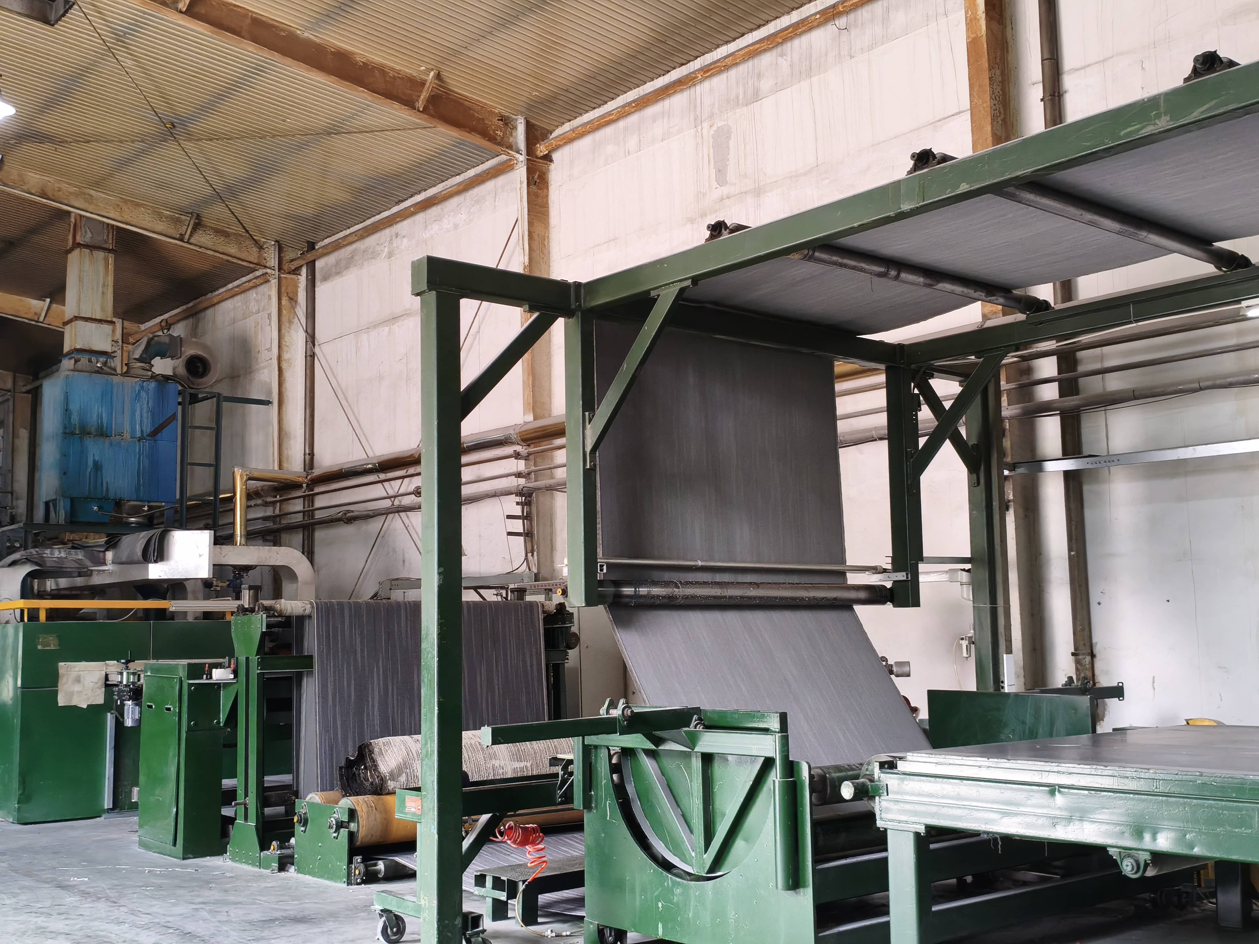 Industrial carpet tile production machine with green frame processing gray fabric in a factory