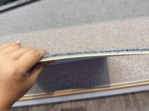 Hand holding a gray custom carpet tile, demonstrating fiber density and pile thickness