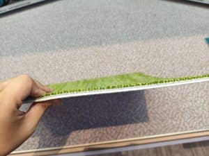 Hand holding a green custom carpet tile, showing pile height and density from a side view