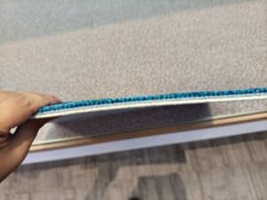 Hand holding a blue custom carpet tile, highlighting the thickness and pile density