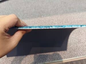 Hand holding a blue custom carpet tile, showing side profile of pile height and density