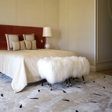 Minimalist bedroom with beige area carpet and white faux-fur bench at bed end